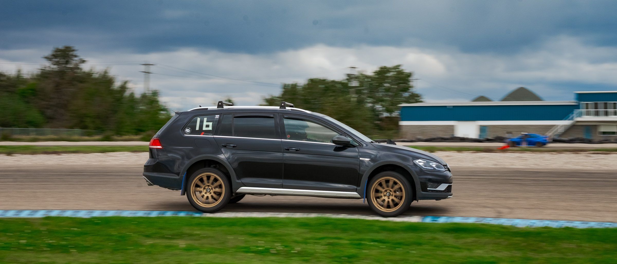 A black wagon cornering at speed on a track under a stormy sky.