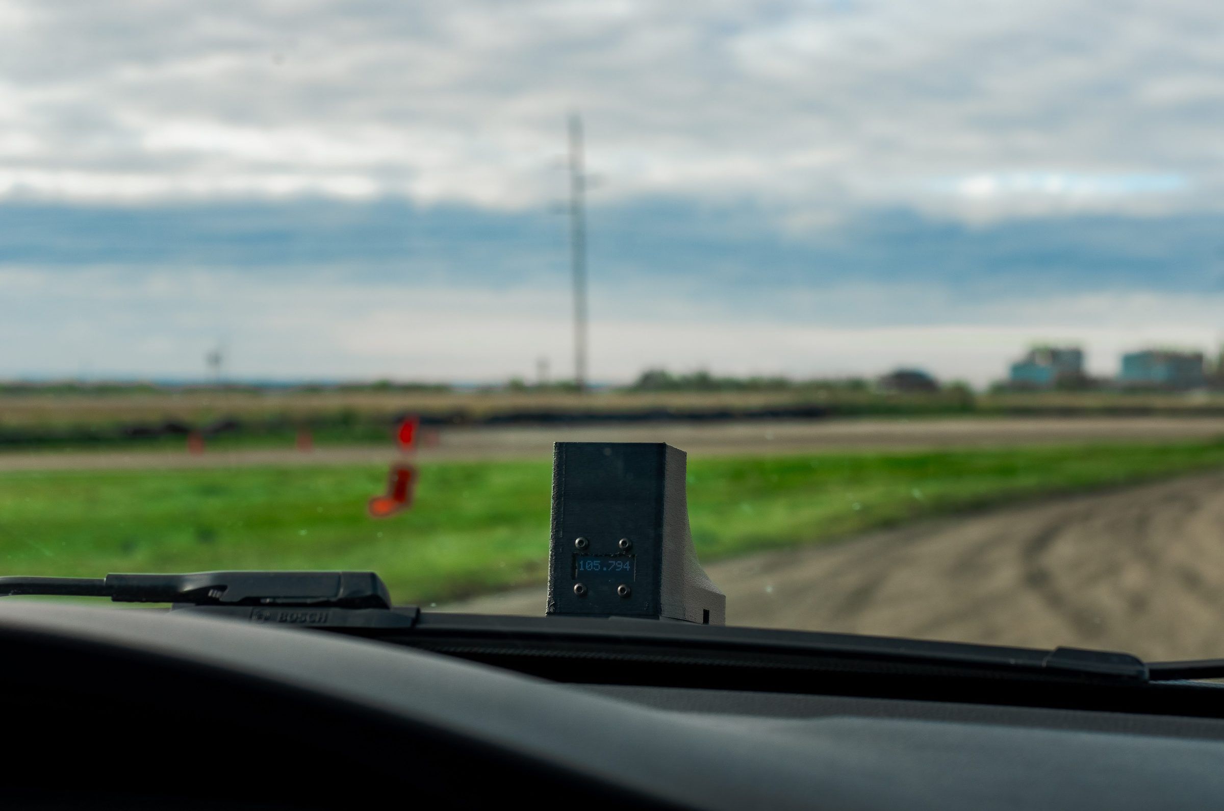 A small timing unit on the hood, seen through the windscreen from the driver's seat, its display showing a lap time.