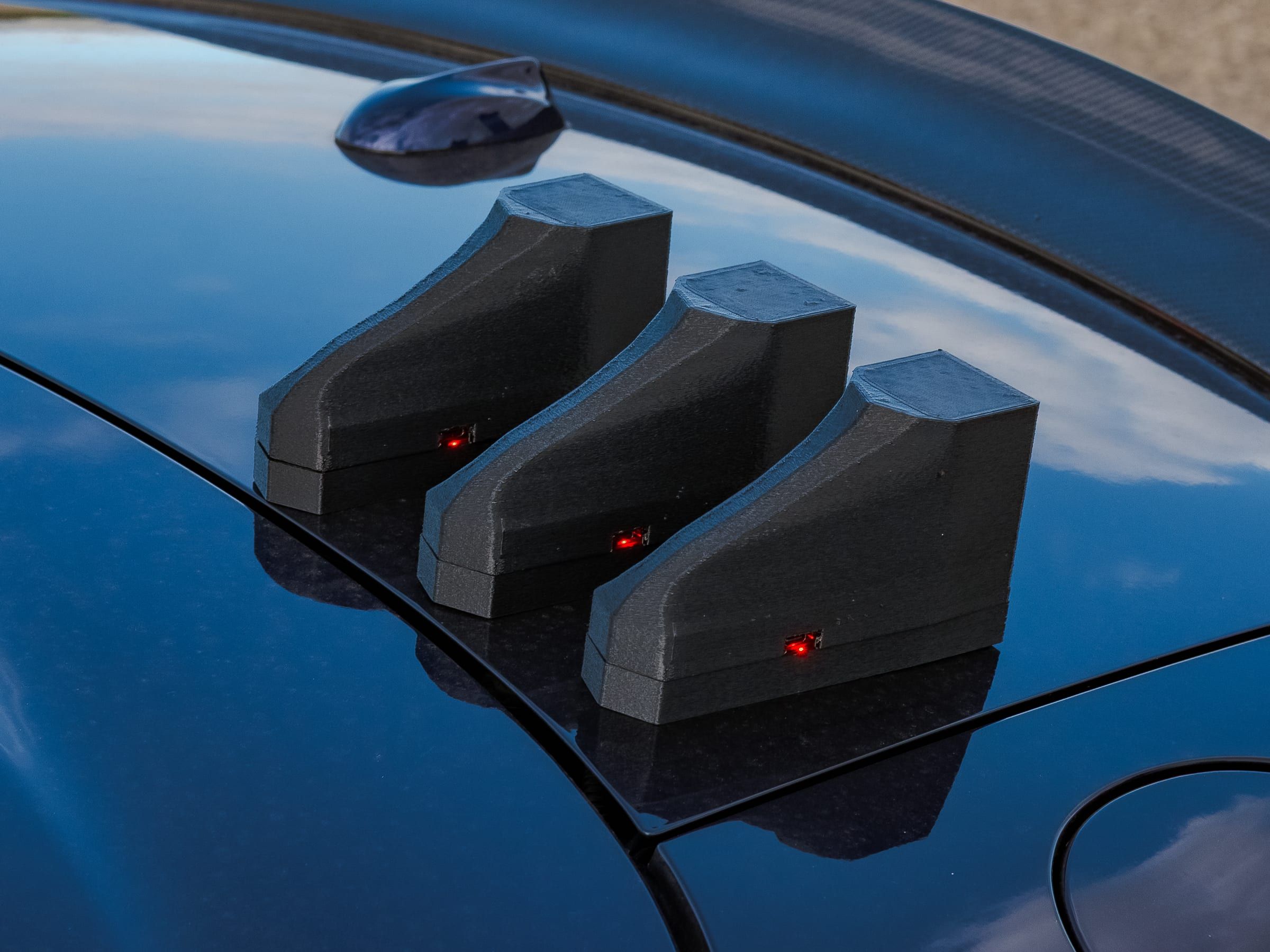 Three timing units on the rear deck of a dark car, beside the spoiler.