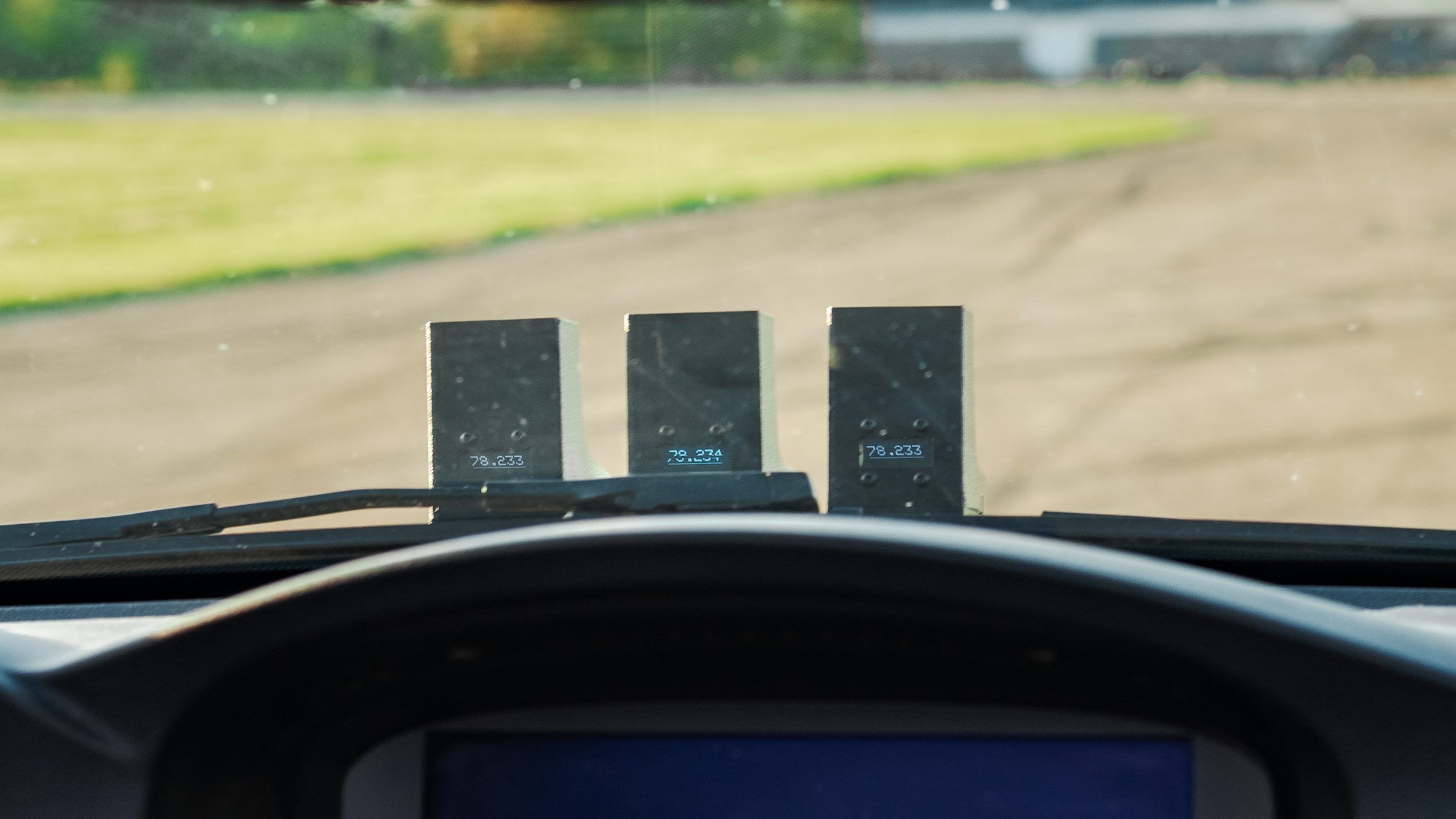 Three timing units on a car dash, seen from the driver's seat, each showing a lap time.