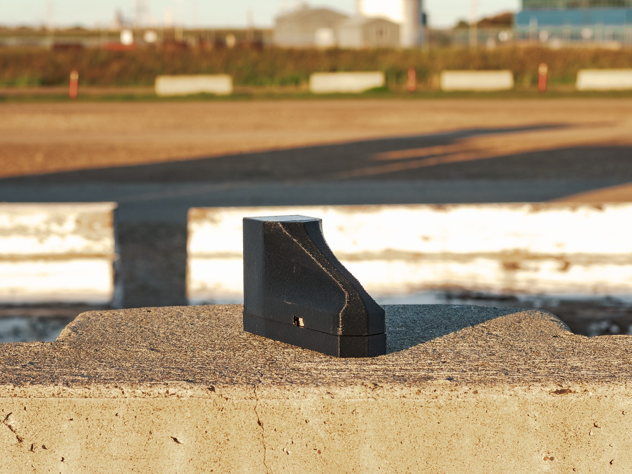 A small black 3D-printed wedge, one of our prototype units, sitting on a concrete barrier in low evening light.