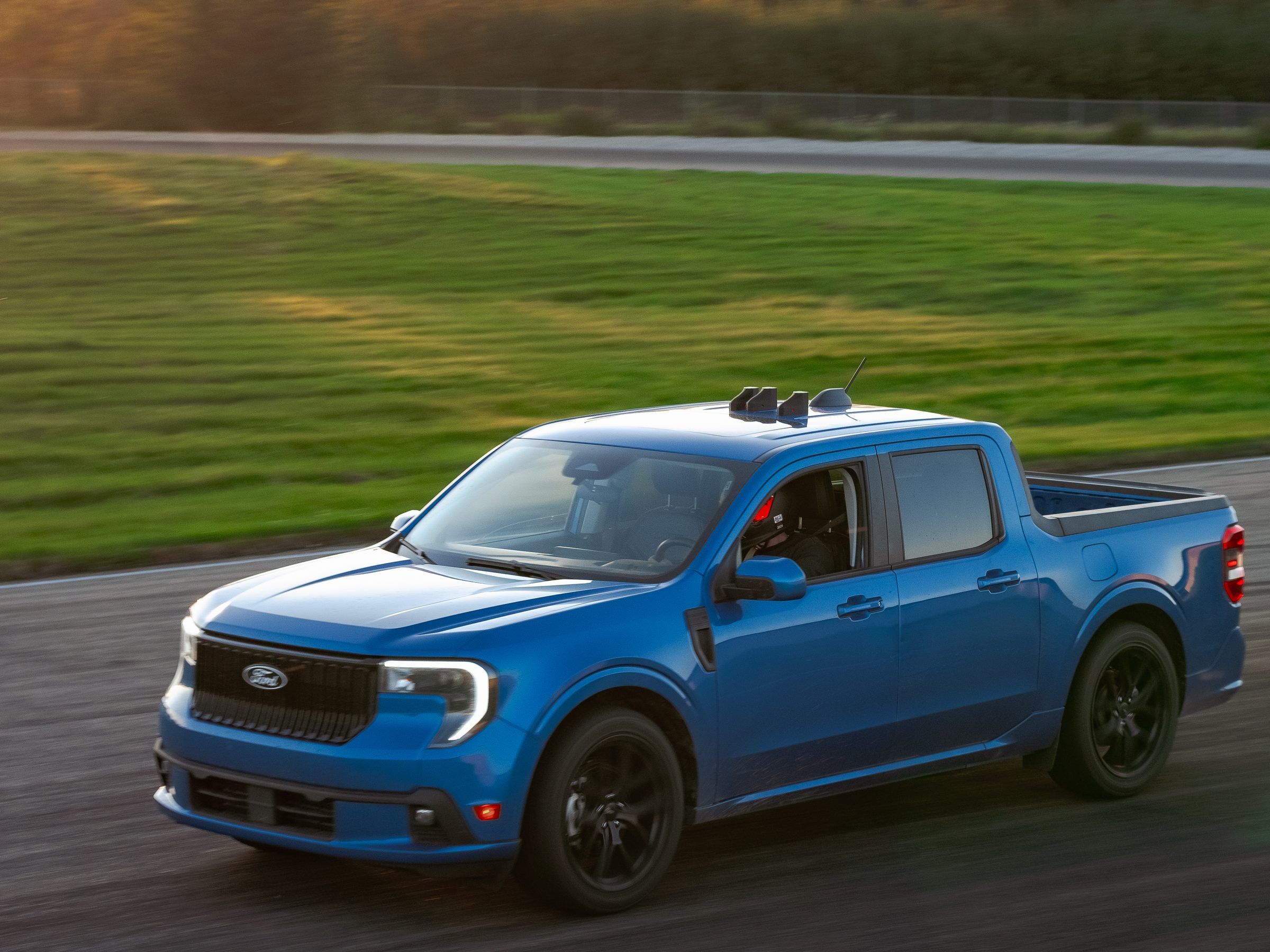 A blue pickup truck cornering on a track at golden hour, with three timing units on its roof.